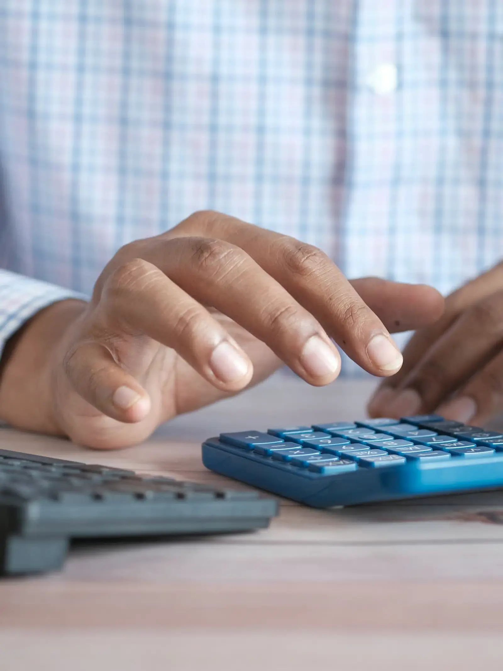 Freelancer's hands totaling figures on a calculator beside a keyboard and coffee, at a tidy desk