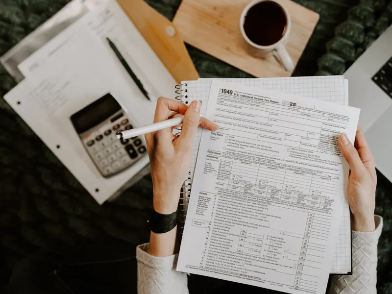 An invoice being filled out by hand next to a calculator, notebook, and coffee at a tidy desk